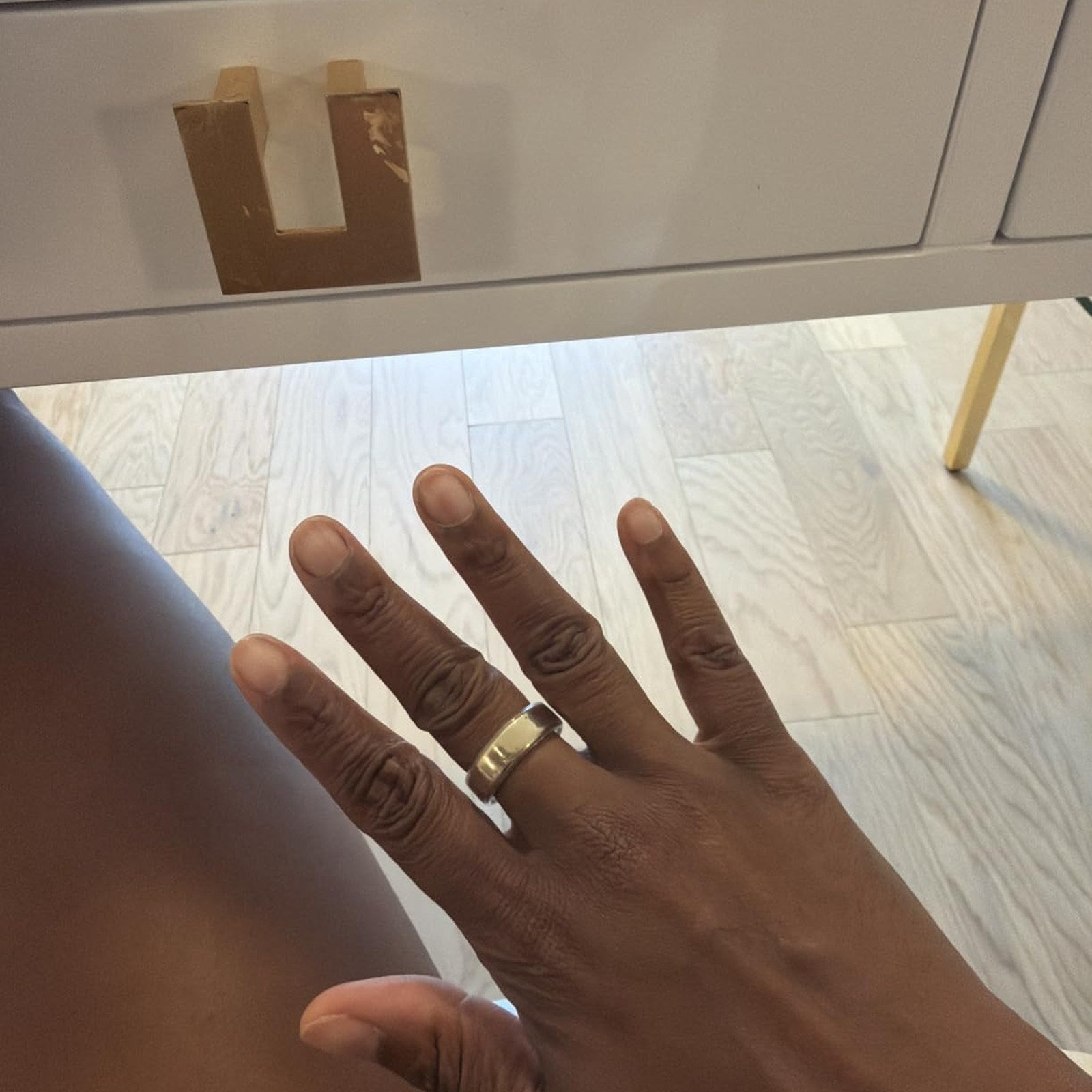 Gold-tone Oura Ring cover worn at home on a dark-skinned hand