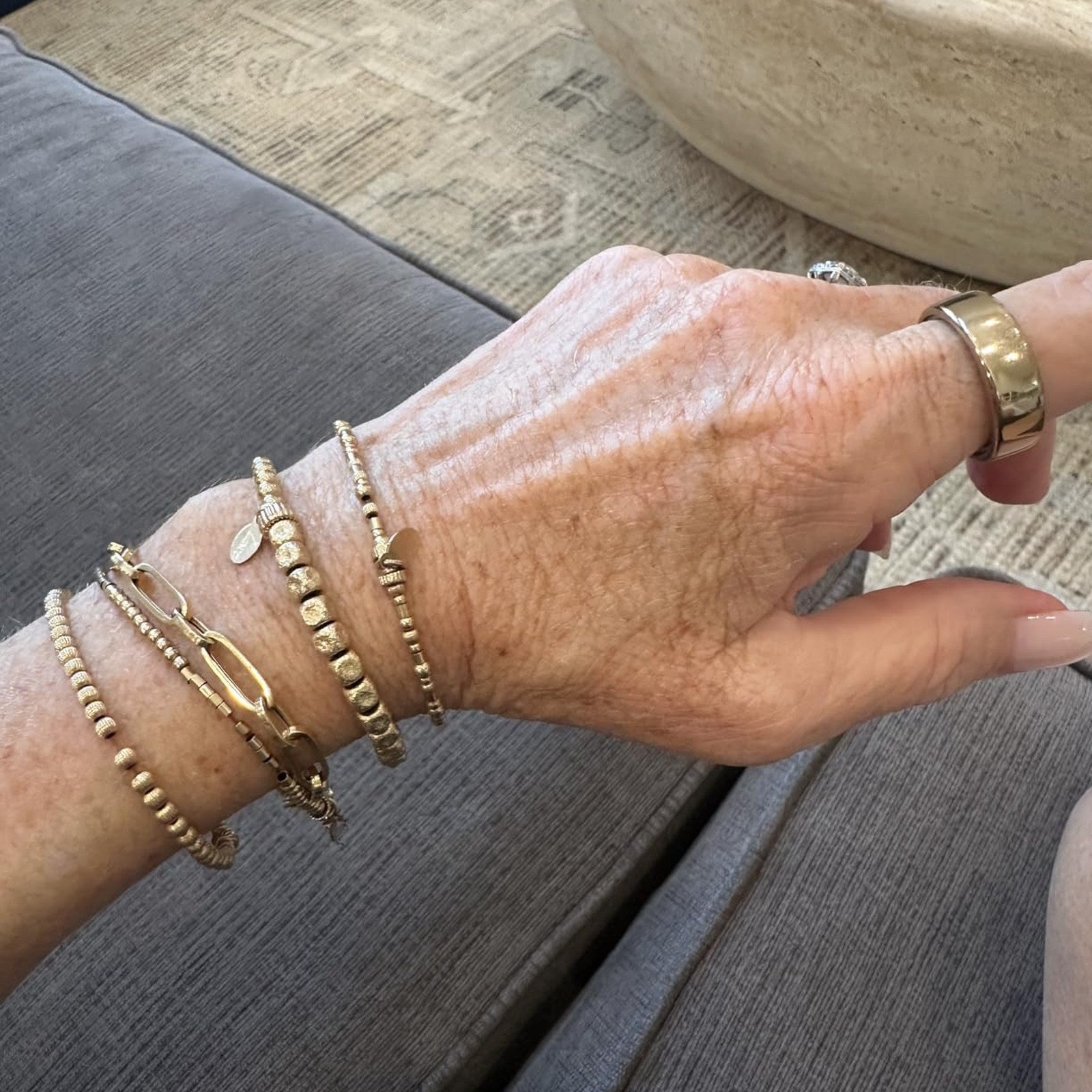 Gold-tone Oura Ring cover worn with layered bracelets at home