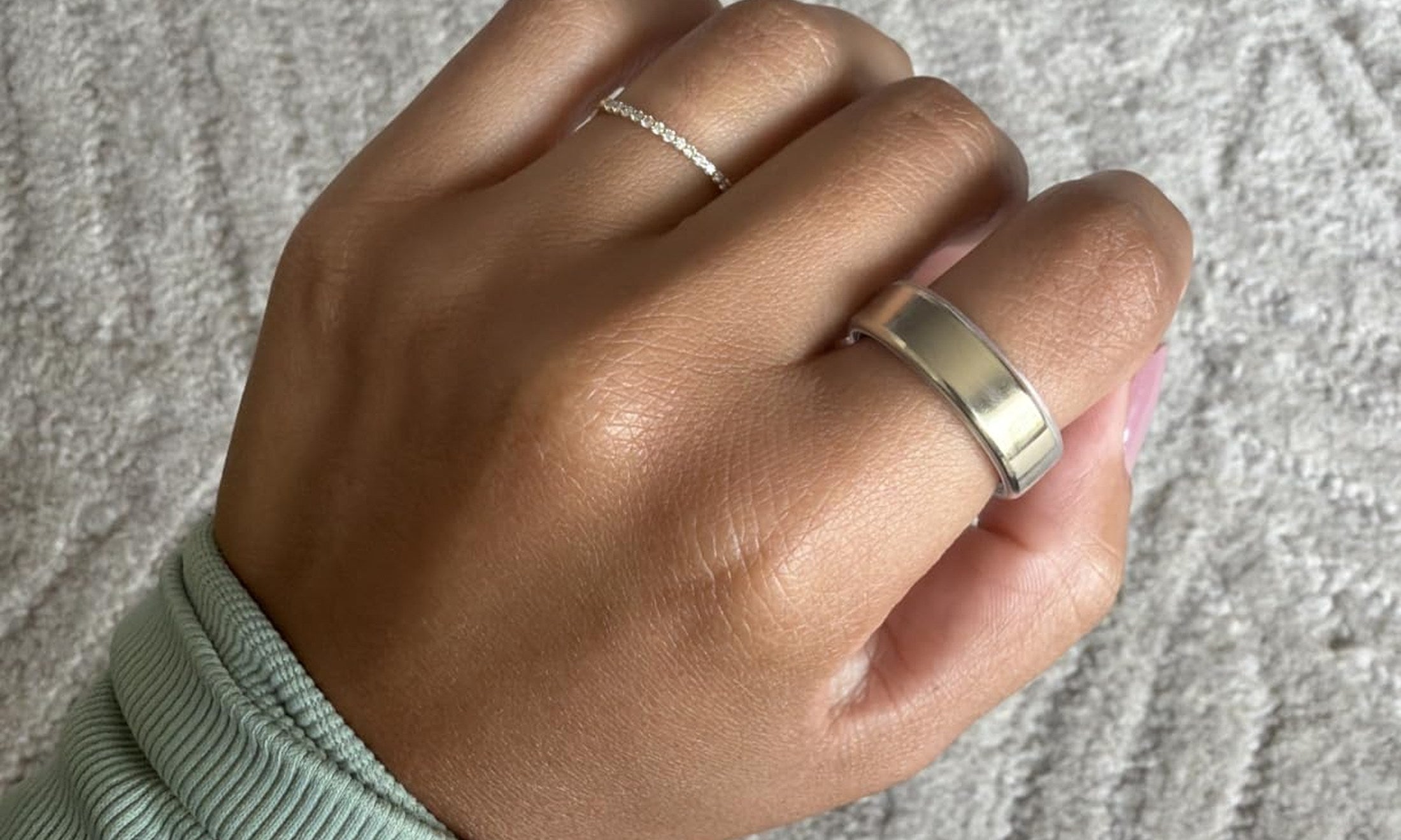 Silver-tone Oura Ring cover worn on a hand with a soft sage sleeve